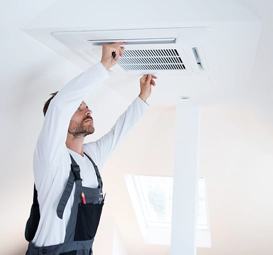 Climatisation : Maintenance et Réparation par un Pro Technicien barbu en combinaison effectuant la maintenance d'une unité de climatisation encastrée au plafond. Il l'ajuste avec un outil.