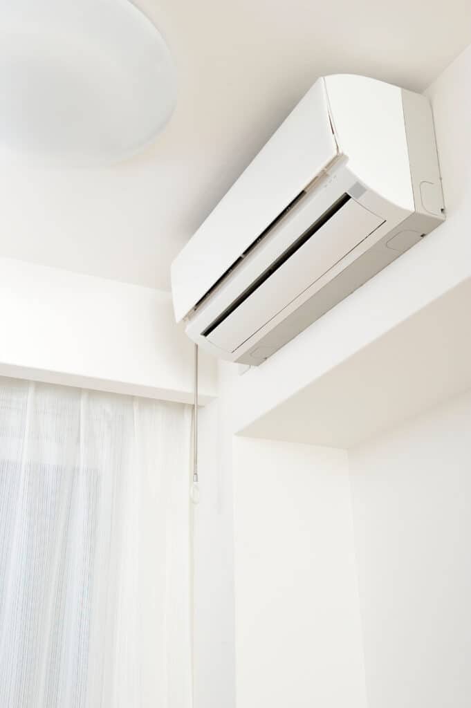 Climatiseur Mural Blanc : Fraîcheur et Confort Intérieur Climatiseur mural blanc fonctionnel dans une pièce claire et moderne, près de rideaux transparents et un plafonnier.