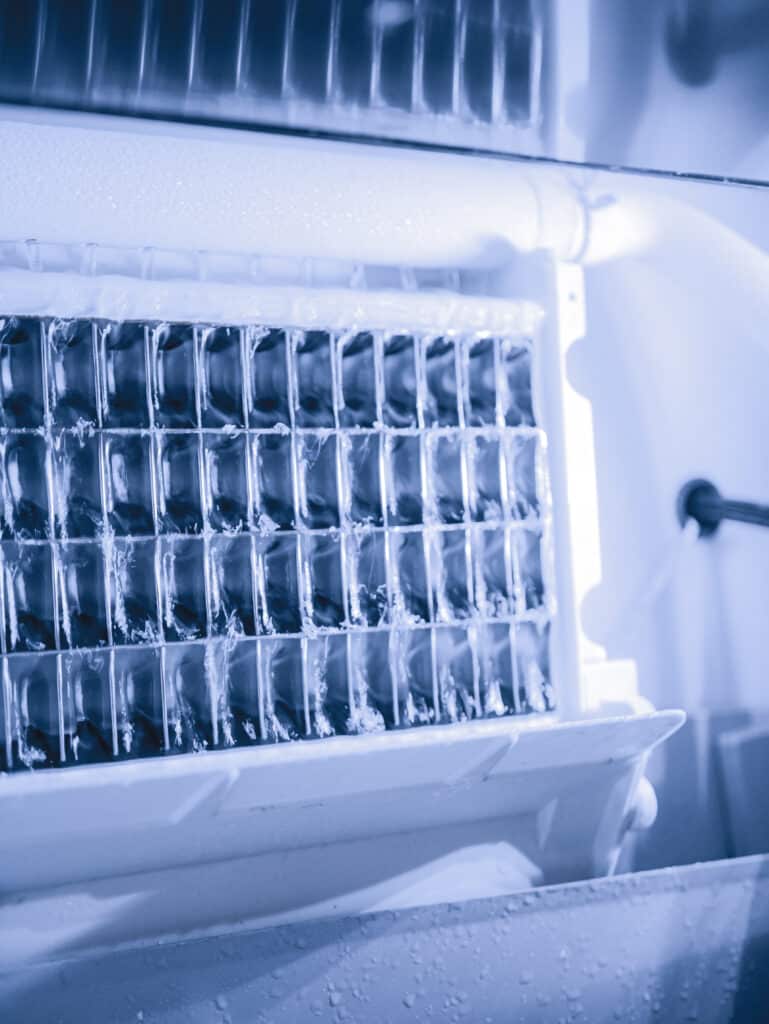 Glaçons frais : Machine à glaçons automatique pour réfrigérateur Glaçons fraîchement formés dans un bac à glaçons automatique de réfrigérateur. L'intérieur givré et bleuté révèle le mécanisme de fabrication de glace.